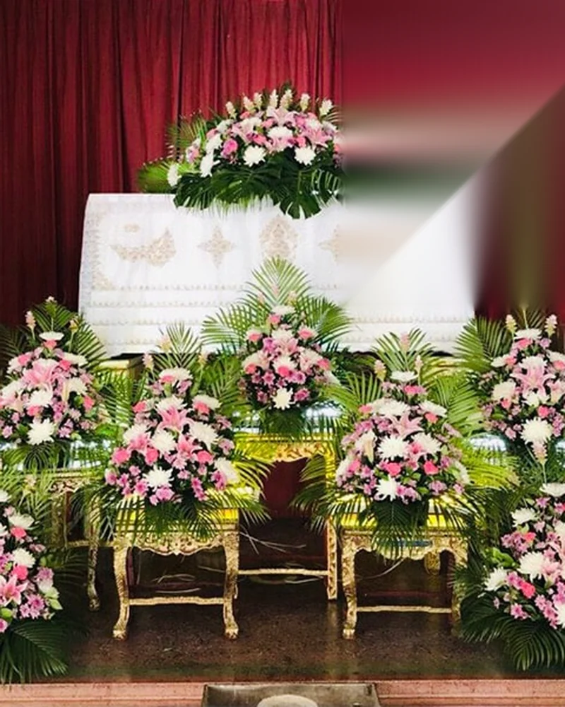 หีบศพลายทองพร้อมดอกไม้โทนชมพูขาวที่จัดไว้หน้าหีบในศาลาวัด