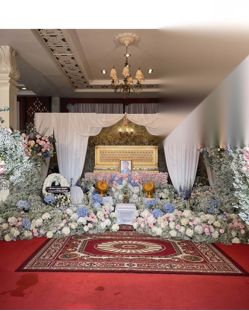 ภายในศาลาวัดที่จัดดอกไม้สีขาวเต็มด้านหน้าและปูพรมสำหรับประกอบพิธี