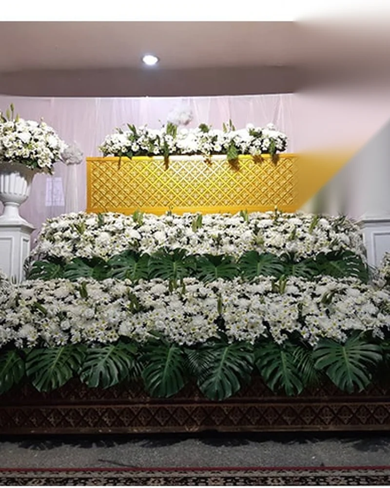 ดอกไม้ไว้อาลัยโทนขาวล้วนที่จัดเป็นแนวยาวด้านหน้าหีบในห้องประกอบพิธี